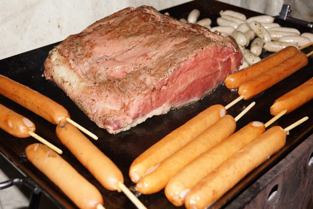 鉄板で焼かれているブロック肉とソーセージ