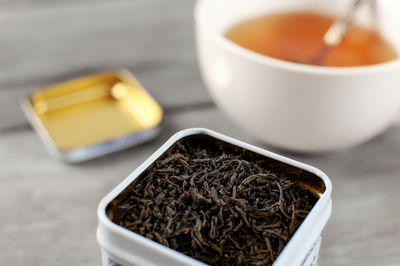 紅茶。Black loose tea in metal tin, with blurred cup of hot amber drink in background.