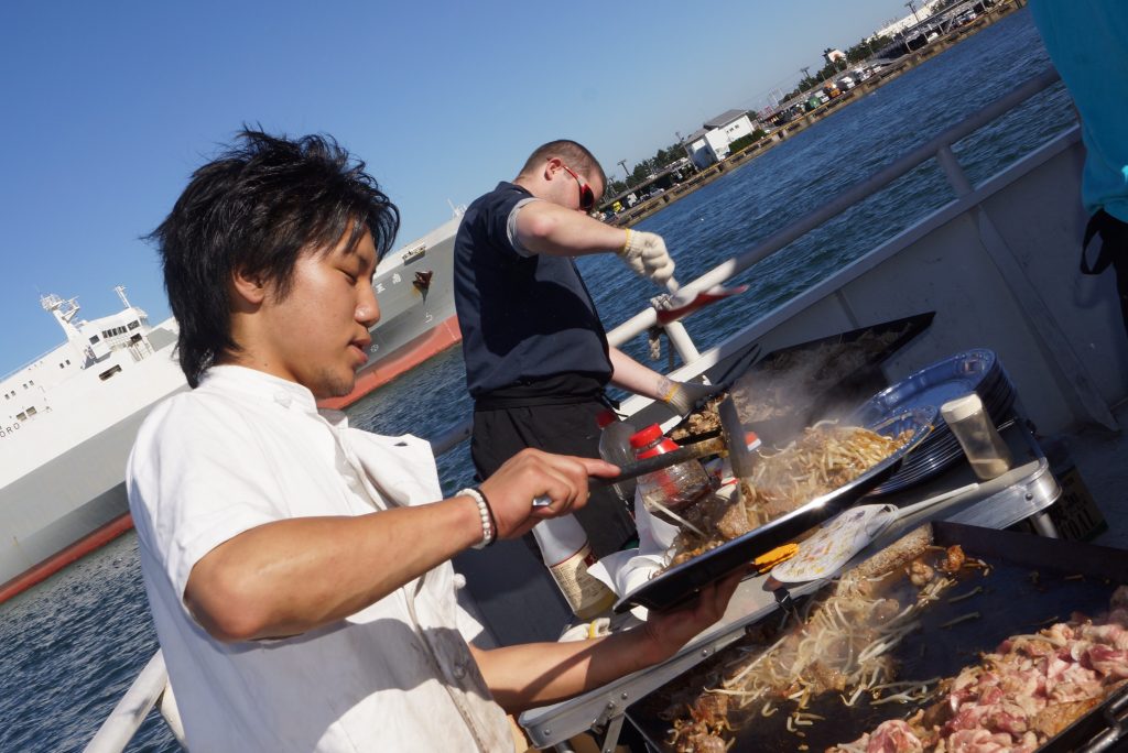 船上でBBQコンロを使って鉄板焼きを行っている風景